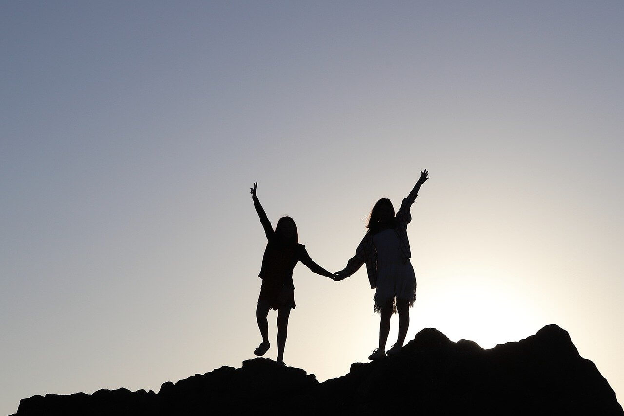 Image of children holding hands happily at the top of a hill with sunlight in the background